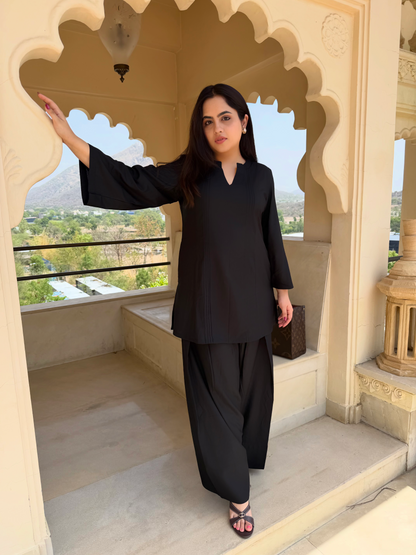 Woman in black farsi salwar suit outfit standing in an ornate architectural setting with scenic view.