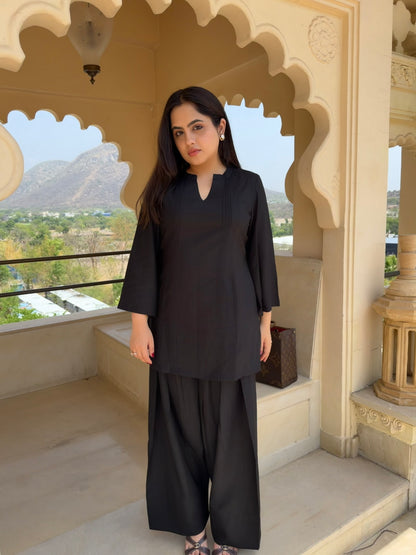 Woman in a black farsi salwar suit  outfit standing in an ornate architectural setting with mountains in the background