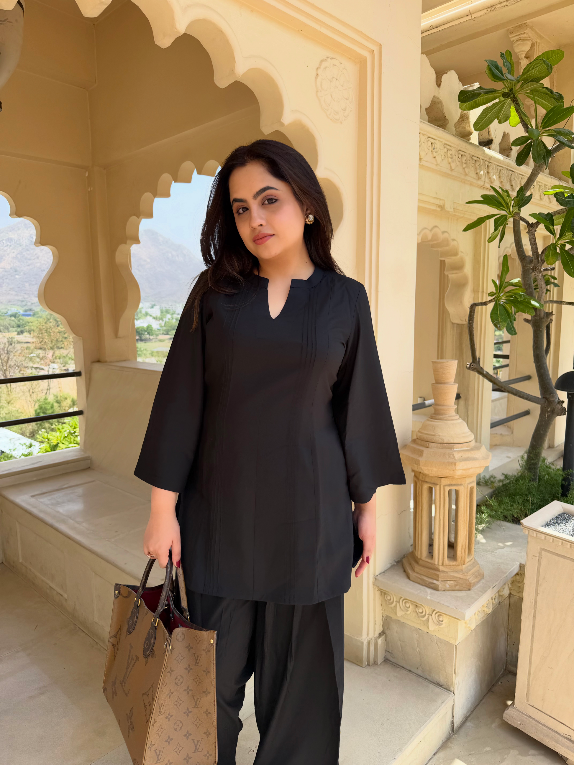 Woman in black farsi salwar suit  outfit holding a brown bag in an ornate architectural setting