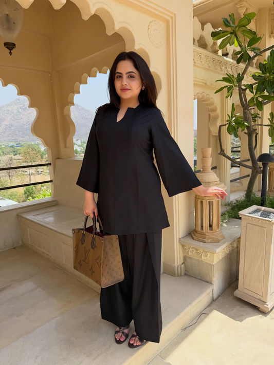 Woman in black outfit farsi salwar suit  standing in a decorative outdoor setting with mountains in the background